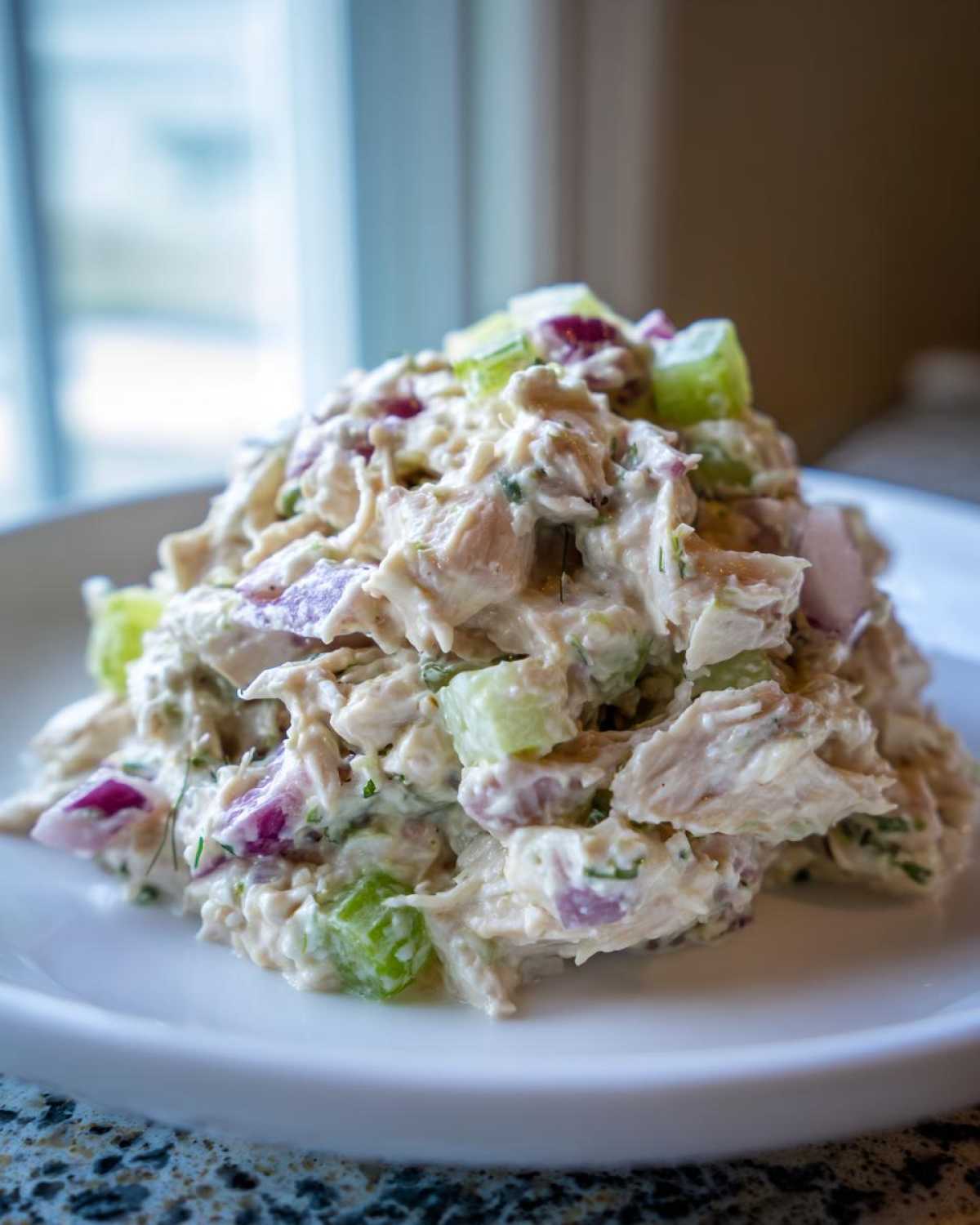 A mound of creamy cottage cheese chicken salad mixed with diced red onion and celery served on a white plate.