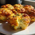 A plate of golden brown cottage cheese egg cups, one with a bite taken out showing the fluffy interior.