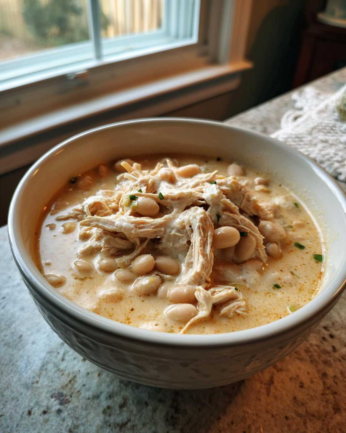 A close-up of a bowl filled with creamy crockpot white chicken chili, featuring shredded chicken and white beans.