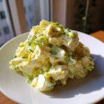 A mound of creamy, chunky egg salad recipe mixed with celery and topped with fresh chives, served on a white plate.
