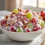 A bowl piled high with creamy chicken salad chick grape salad, featuring red and green grapes coated in dressing and topped with chopped pecans.