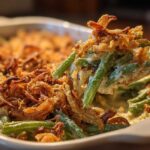 A spoonful of creamy green bean casserole topped with crispy fried onions being lifted from the baking dish.