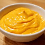 A close-up of thick, vibrant orange homemade nacho cheese sauce in a small white bowl.