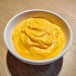Close-up of thick, vibrant orange homemade nacho cheese sauce swirled in a small white dipping bowl.