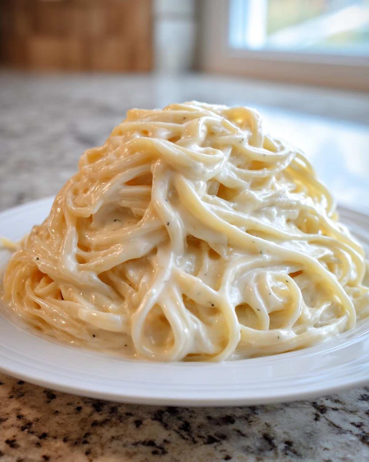 A mound of spaghetti generously coated in creamy homemade alfredo sauce, served on a white plate.