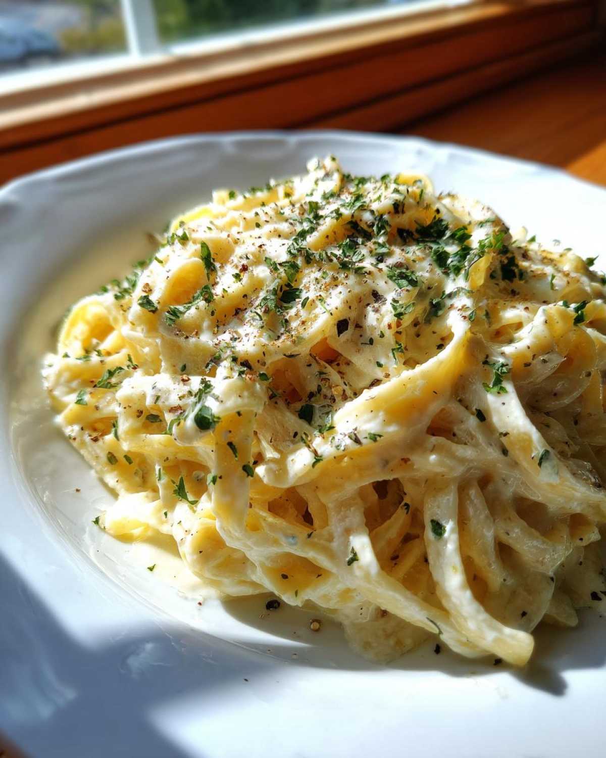 Close-up of fettuccine pasta coated in rich, creamy Olive Garden Alfredo Sauce, topped with parsley.