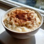 A close-up of creamy rice pudding in a white bowl, generously sprinkled with cinnamon.
