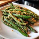 A close-up of bright green beans topped with crispy breadcrumbs and salt, served on a white plate.