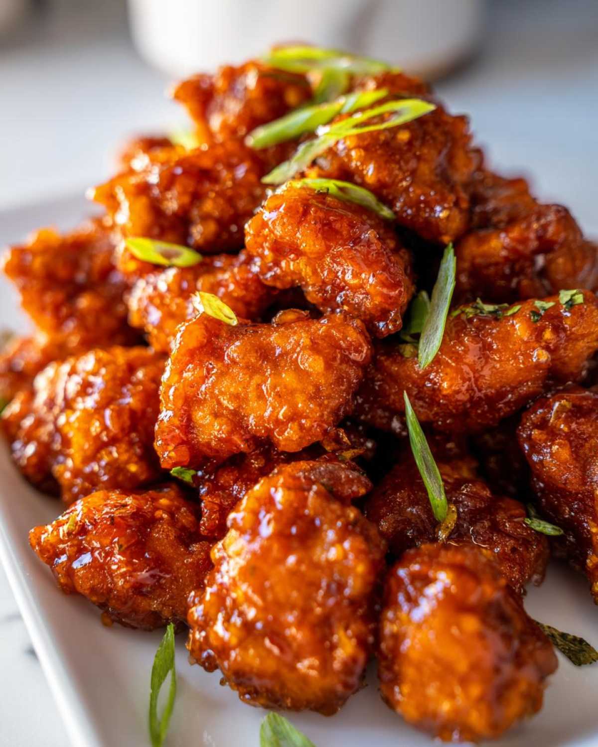 Close-up of crispy, glazed pieces of orange chicken recipe piled high and garnished with sliced green onions.