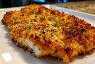 Close-up of a perfectly cooked, golden brown parmesan crusted chicken fillet showing a juicy white interior.