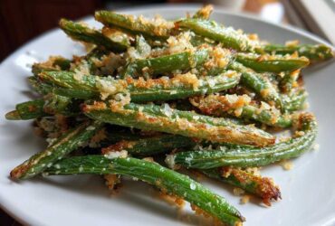 A close-up of crispy, roasted green beans topped with golden parmesan breadcrumbs.
