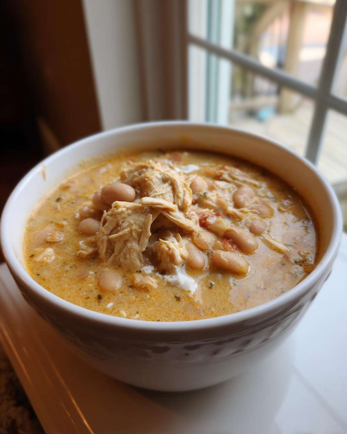 A close-up of a white bowl filled with creamy crockpot white chicken chili, featuring shredded chicken and white beans.