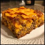 A thick slice of Dorito Casserole featuring layers of seasoned ground beef, creamy cheese sauce, and a topping of melted cheese and crushed Doritos.