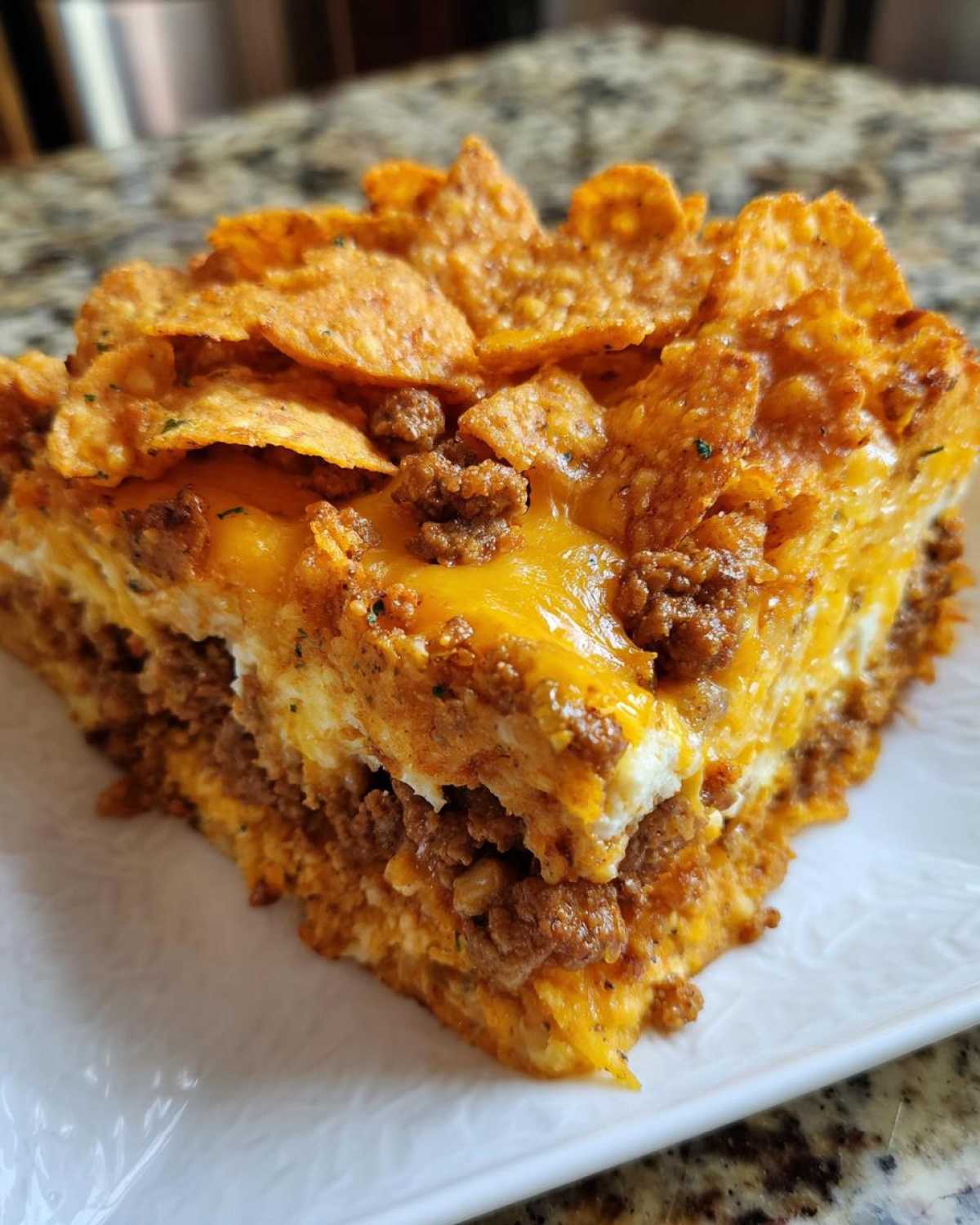 A close-up slice of Dorito Casserole featuring layers of seasoned ground meat, melted cheese, and a crunchy Dorito topping.