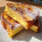 Close-up of three thick slices of golden brown easy french toast dusted heavily with powdered sugar.