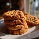 A stack of four golden brown Easy Peanut Butter Cookies showing classic crisscross fork marks, sitting on a white plate.