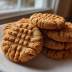 A stack of freshly baked Easy Peanut Butter Cookies featuring classic crisscross fork marks, served on a white plate.