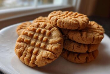 A stack of freshly baked Easy Peanut Butter Cookies featuring classic crisscross fork marks, served on a white plate.