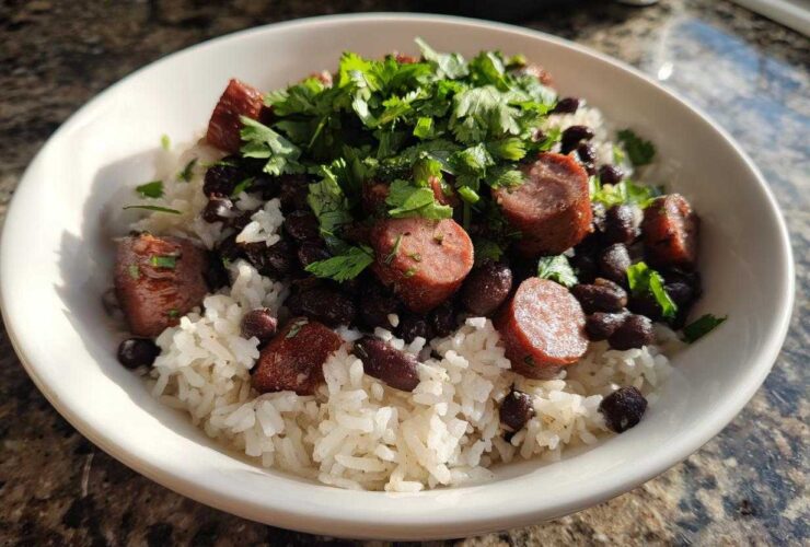 A white bowl filled with white rice, black beans and rice, sliced sausage, and topped with fresh cilantro.