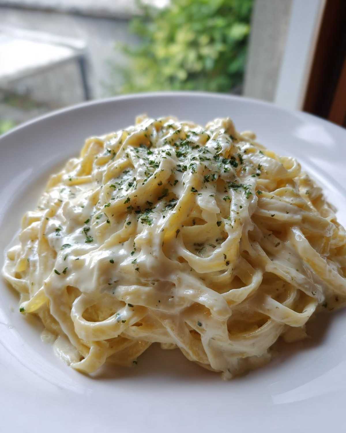 Close-up of fettuccine pasta generously coated in creamy Olive Garden Alfredo Sauce and topped with parsley.