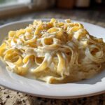 A close-up of fettuccine pasta generously coated in creamy homemade alfredo sauce and topped with black pepper.