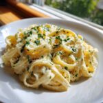 A close-up of fettuccine pasta coated in rich Olive Garden Alfredo Sauce, topped with Parmesan and parsley.