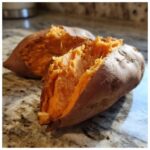 Close-up of a perfectly baked sweet potato split open, revealing its soft, bright orange flesh.