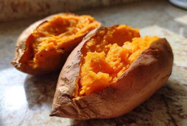 Close-up of a perfectly baked sweet potato split open, revealing its bright orange, fluffy interior.