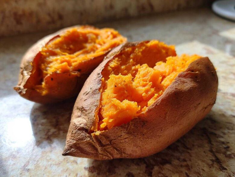 Close-up of a perfectly baked sweet potato split open, revealing its bright orange, fluffy interior.