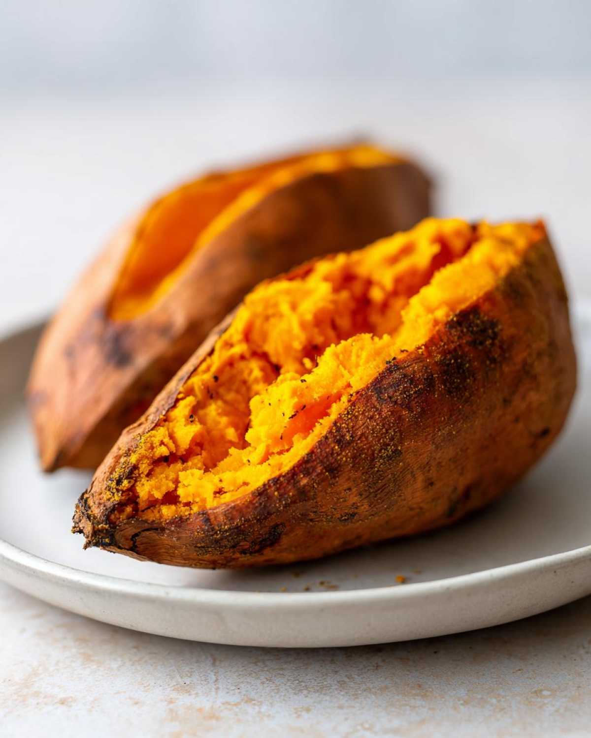 Close-up of two halves of perfectly baked sweet potatoes showing fluffy, bright orange interior.