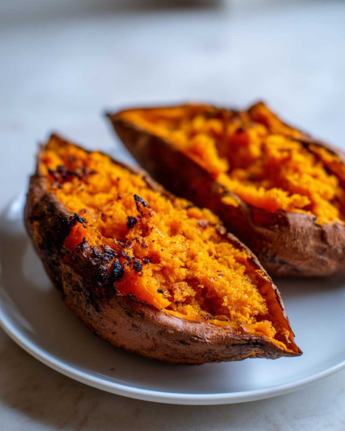 Two halves of perfectly cooked baked sweet potatoes showing bright orange, fluffy interiors on a white plate.