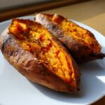 Two perfectly baked sweet potatoes, split open to show the fluffy orange interior seasoned with dark herbs.