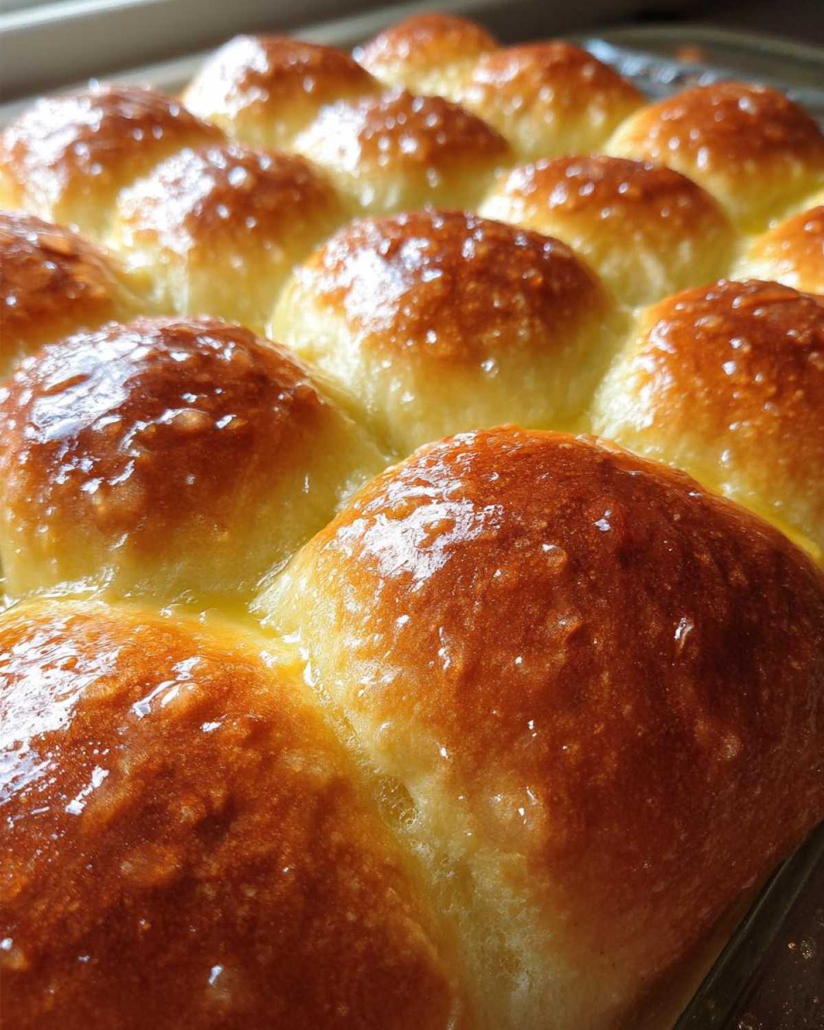 Close-up of golden brown, fluffy dinner rolls brushed with melted butter.