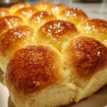 Close-up of freshly baked, fluffy dinner rolls with a shiny, buttery glaze on top.