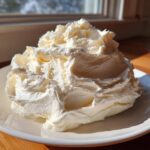 A large, fluffy mound of freshly made cream cheese frosting piled high on a white plate.