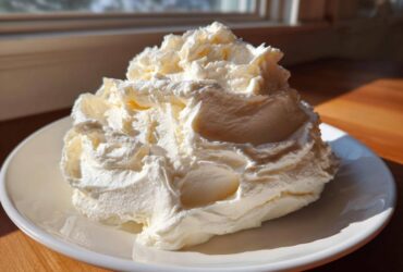 A large, fluffy mound of freshly made cream cheese frosting piled high on a white plate.