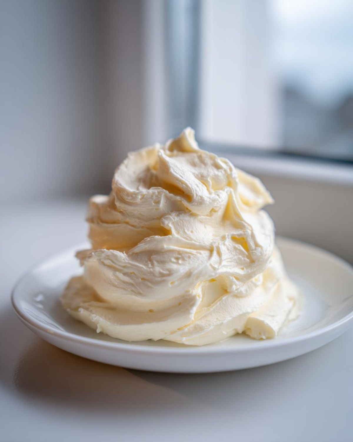 A generous swirl of fluffy, pale yellow cream cheese frosting piled high on a small white plate.