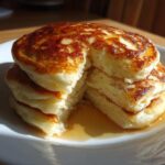 A tall stack of four fluffy greek yogurt pancakes, drizzled with syrup and cut open to show the texture.