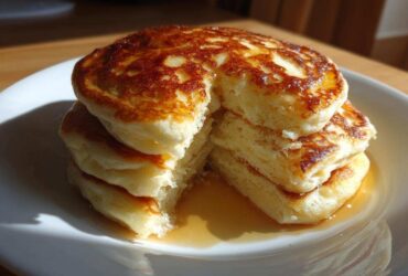 A tall stack of four fluffy greek yogurt pancakes, drizzled with syrup and cut open to show the texture.