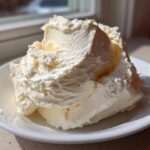 A generous dollop of light, fluffy vanilla buttercream frosting piled high on a small white plate.
