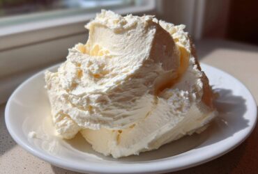 A generous dollop of light, fluffy vanilla buttercream frosting piled high on a small white plate.