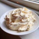 A mound of freshly made, fluffy vanilla buttercream frosting swirled high on a small white plate.