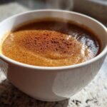 Close-up of warm applesauce in a white bowl, topped with ground cinnamon.
