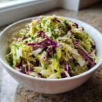 A white bowl filled with vibrant cabbage salad featuring shredded green and red cabbage, topped with fresh parsley.