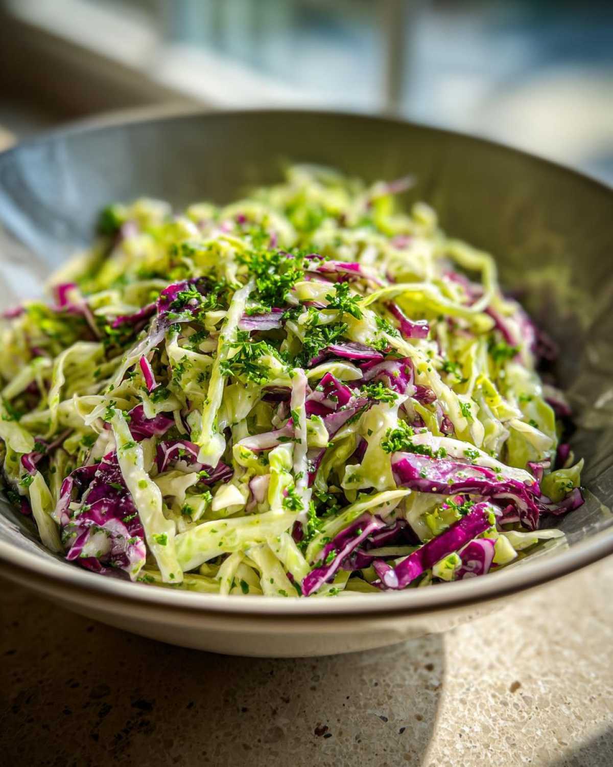 Close-up of a vibrant cabbage salad featuring shredded green and purple cabbage tossed in a light dressing and topped with fresh parsley.
