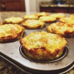 Close-up of golden-brown, cheesy Egg Muffin Cups cooling in a metal muffin tin.