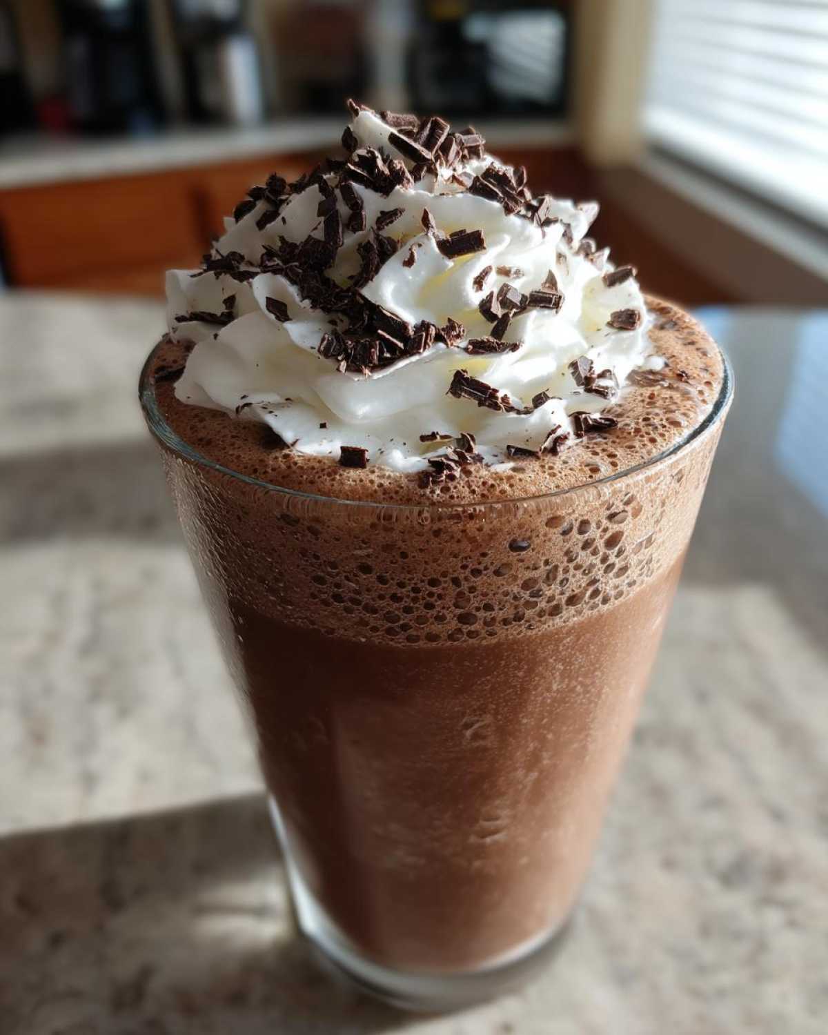 A tall glass of blended frozen hot chocolate topped with whipped cream and chocolate shavings.