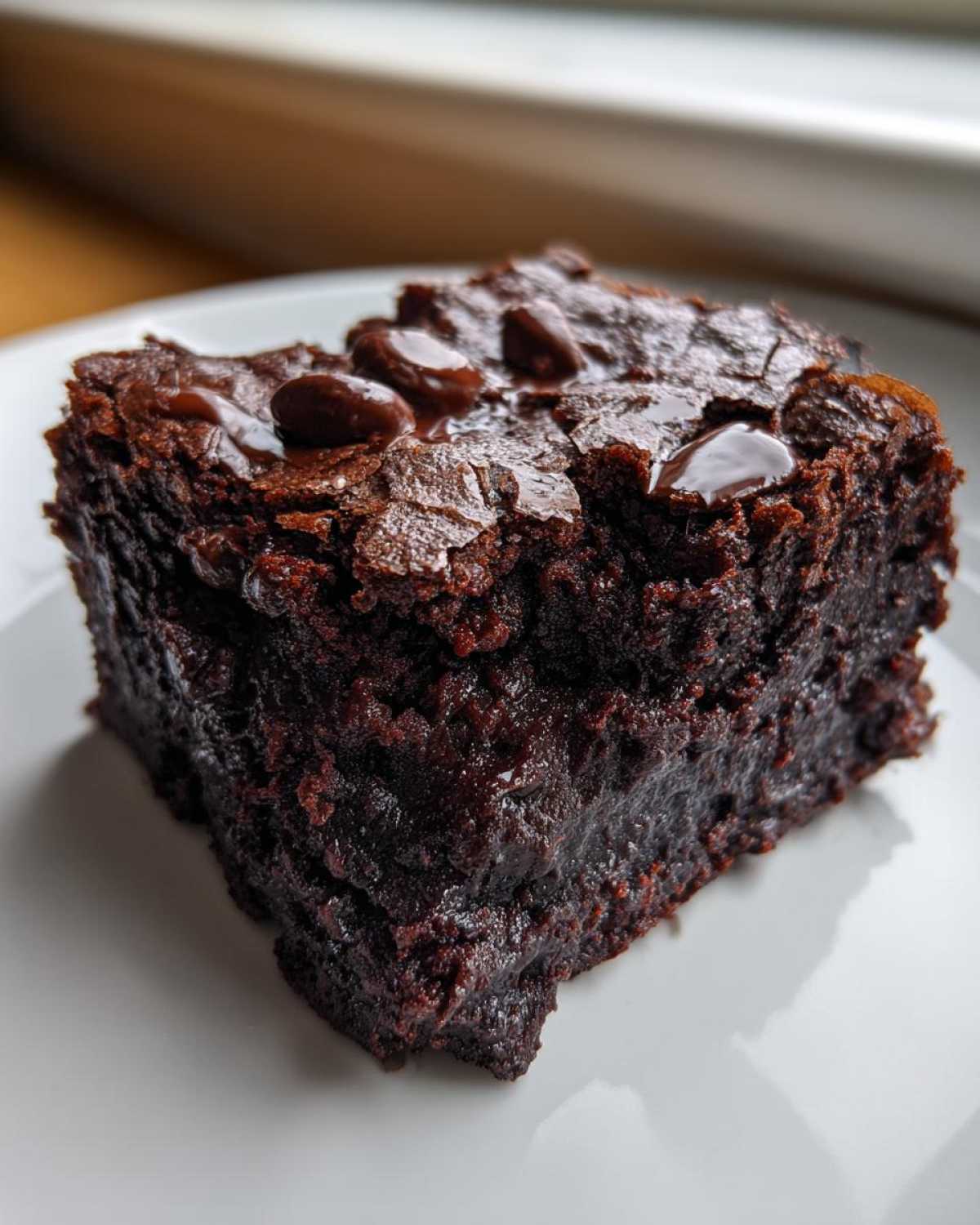 Close-up of a rich, fudgy slice of black bean brownies topped with melted chocolate chips on a white plate.