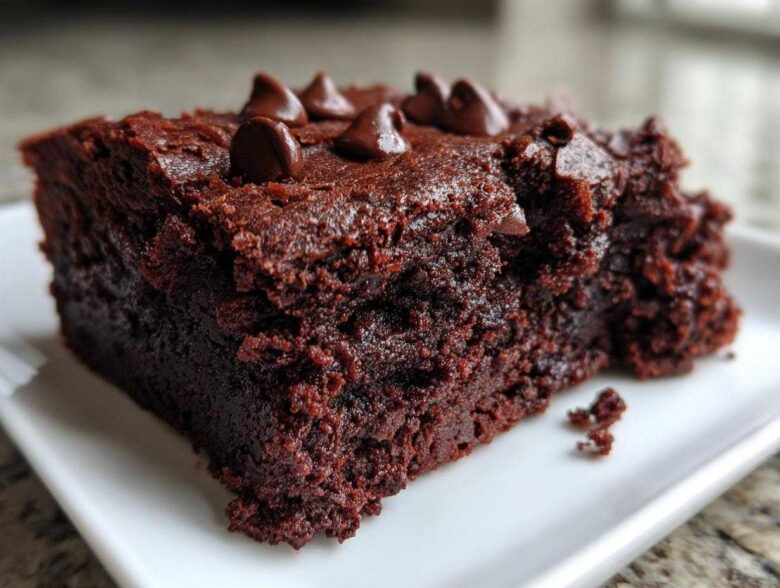 A close-up of a rich, dark, fudgy sweet potato brownies slice topped with chocolate chips.