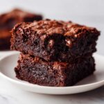 Two stacked, fudgy sweet potato brownies showing a rich, dark chocolate interior and melted chocolate chips.